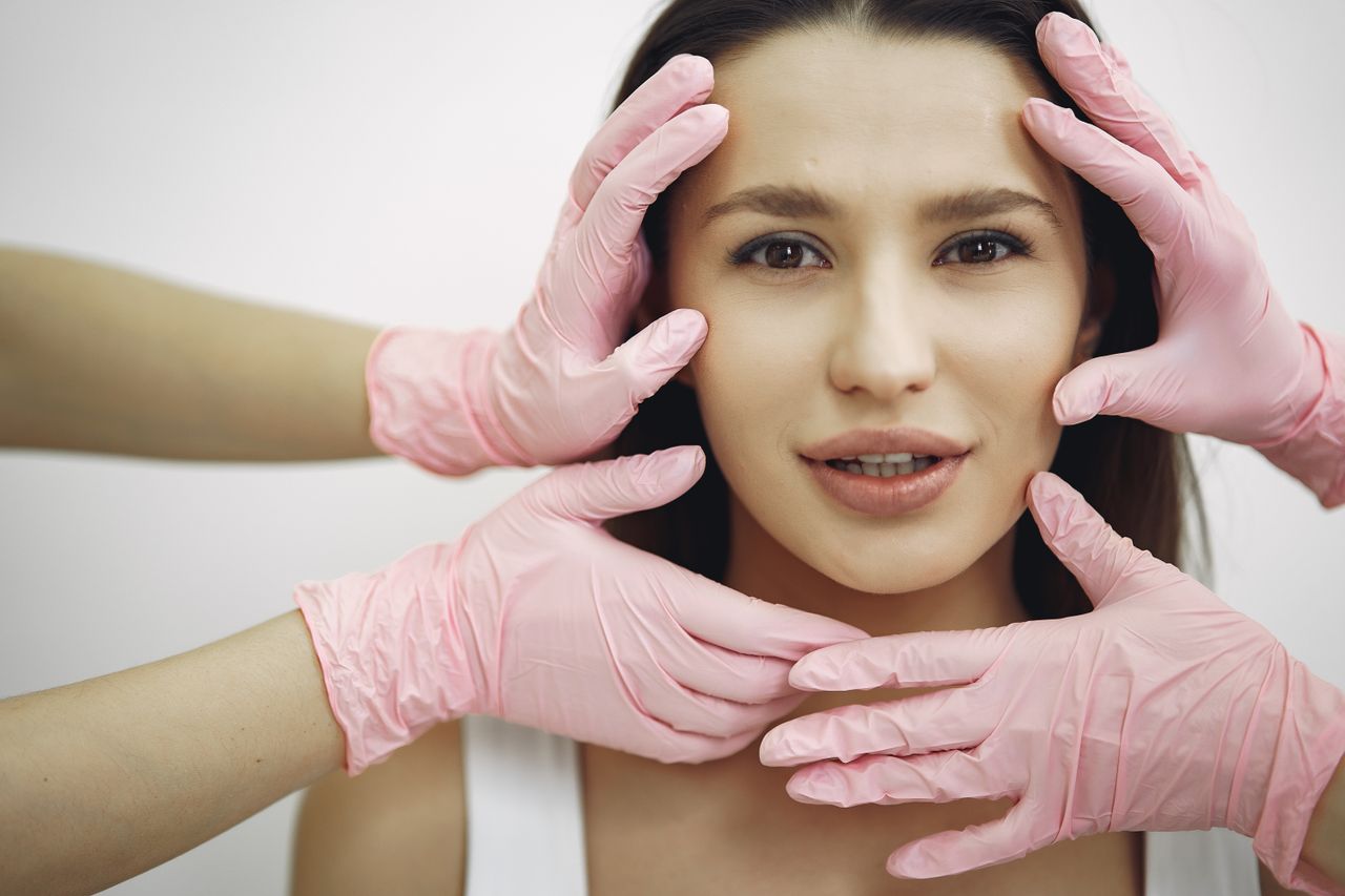 services-01 A woman receiving a facial treatment, hands in gloves gently touching her face indoors.